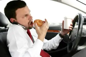 Young male eating a bagel and drinking coffee while driving